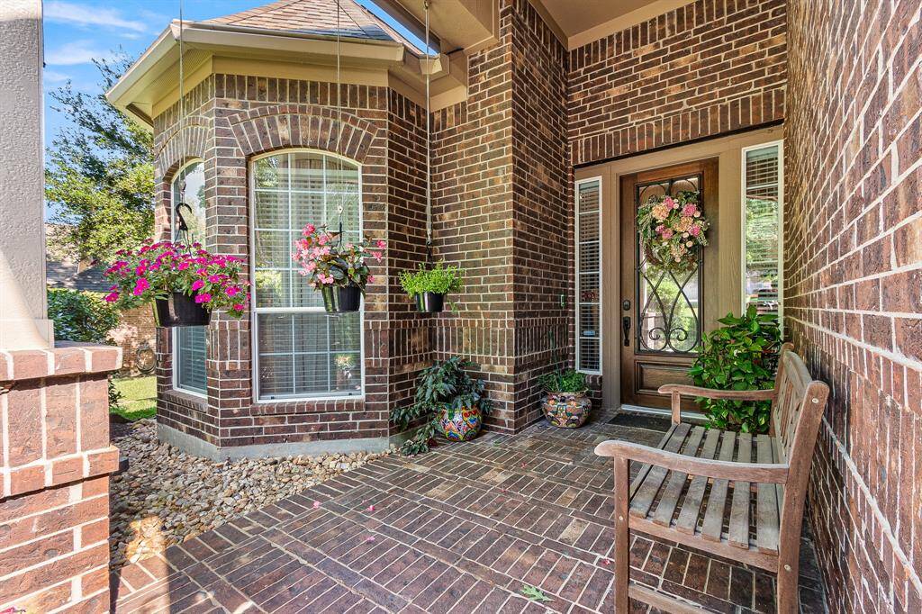 This inviting home entrance features a charming covered brick entrance. The area is adorned with vibrant potted plants and hanging baskets, creating a warm and welcoming atmosphere. Your guest will feel at Home.