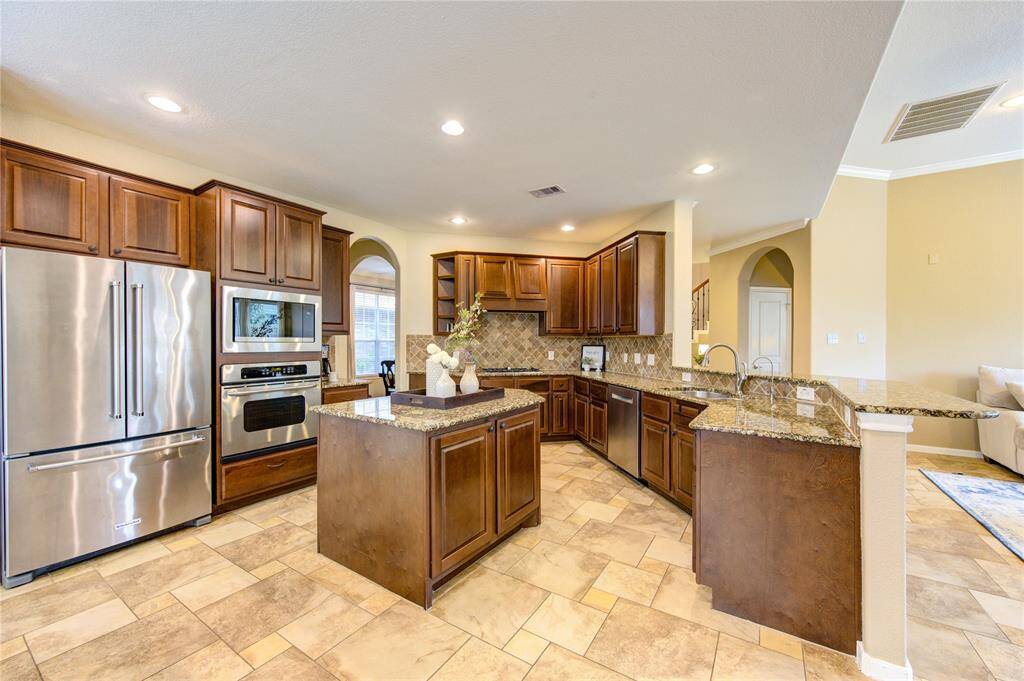 This chef-inspired kitchen boasts rich wood cabinetry, granite countertops, stainless steel appliances, and a wraparound breakfast bar with pendant lighting.