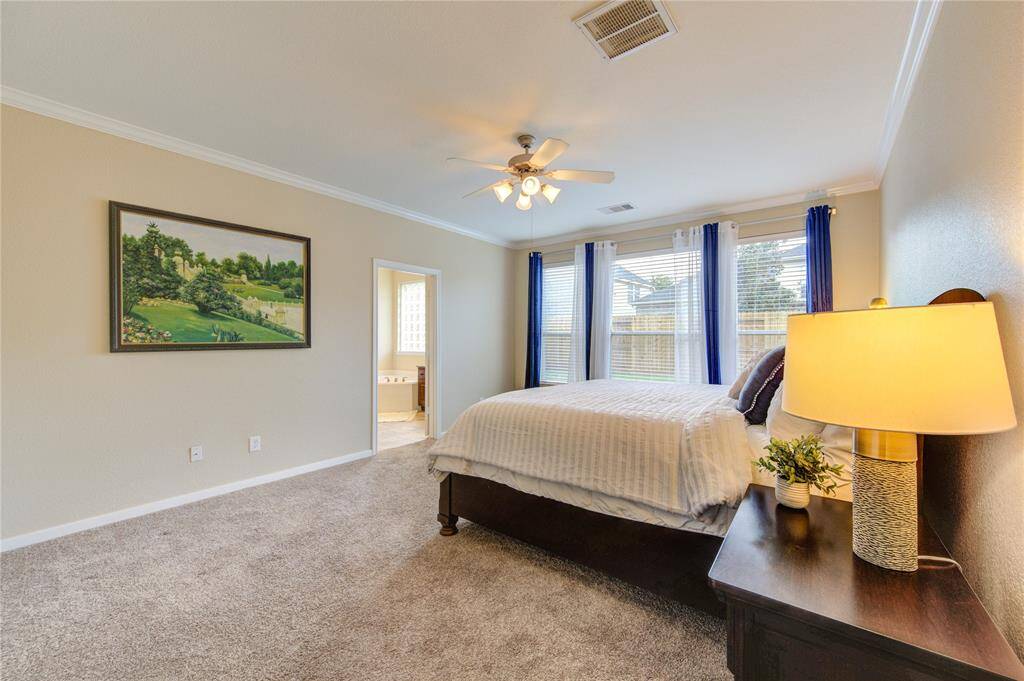 The spacious primary suite is privately tucked away on the main floor, offering a quiet escape with plush carpet, a tray ceiling, and peaceful backyard views through large windows.