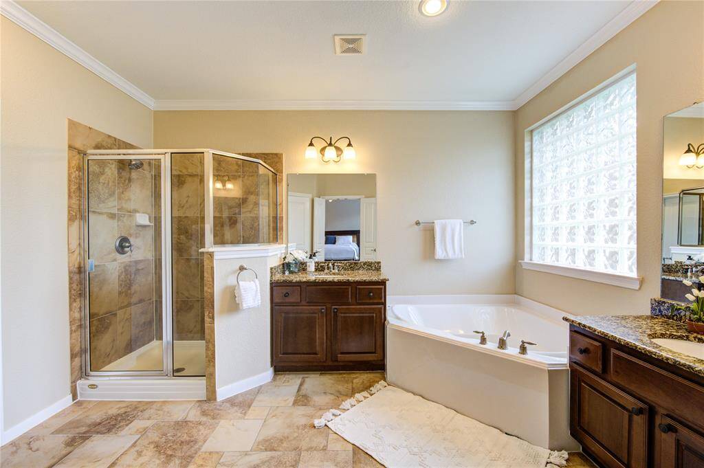 Unwind in the spa-like primary bath featuring dual granite vanities, a deep soaking tub, separate glass-enclosed shower, and a large walk-in closet with built-in shelving for optimal organization.