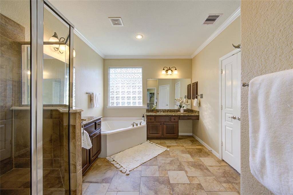 This luxurious primary bathroom is designed for ultimate relaxation and convenience. It features his and her vanities with plenty of counter space for organization, as well as a separate soaking tub for unwinding and a spacious walk-in shower with elegant tile work. The thoughtful layout and modern finishes make this a true spa-like retreat.