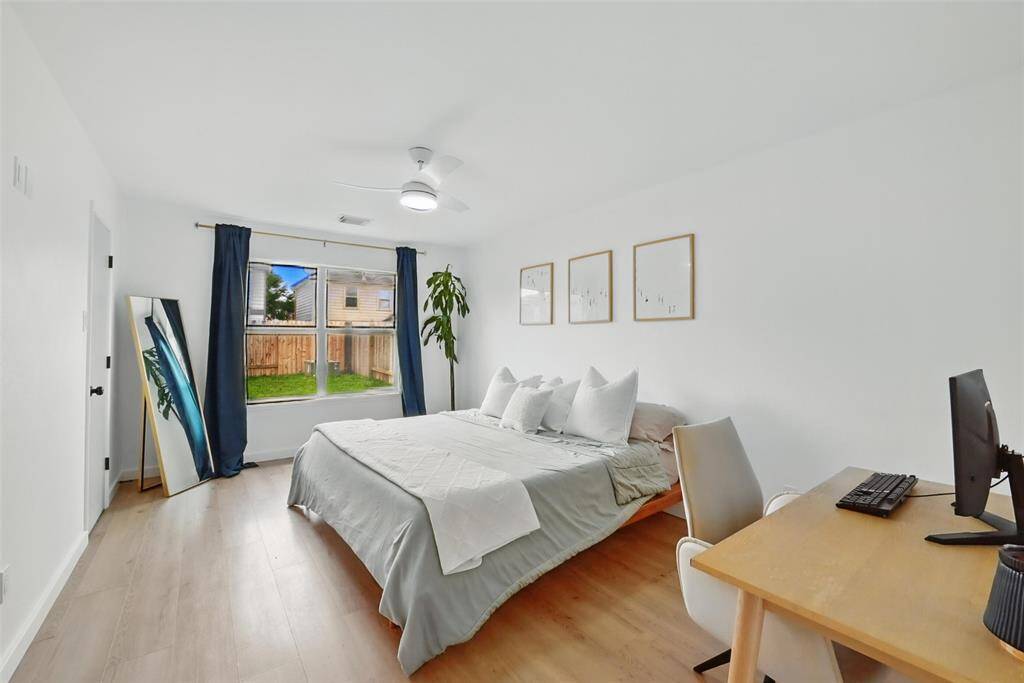 THE PRIMARY SUITE FEATURES LARGE PICTURE WINDOW OVER-LOOKING THE SERENE BACKYARD. NOTICE THE CHIC MODERN CEILING FAN.