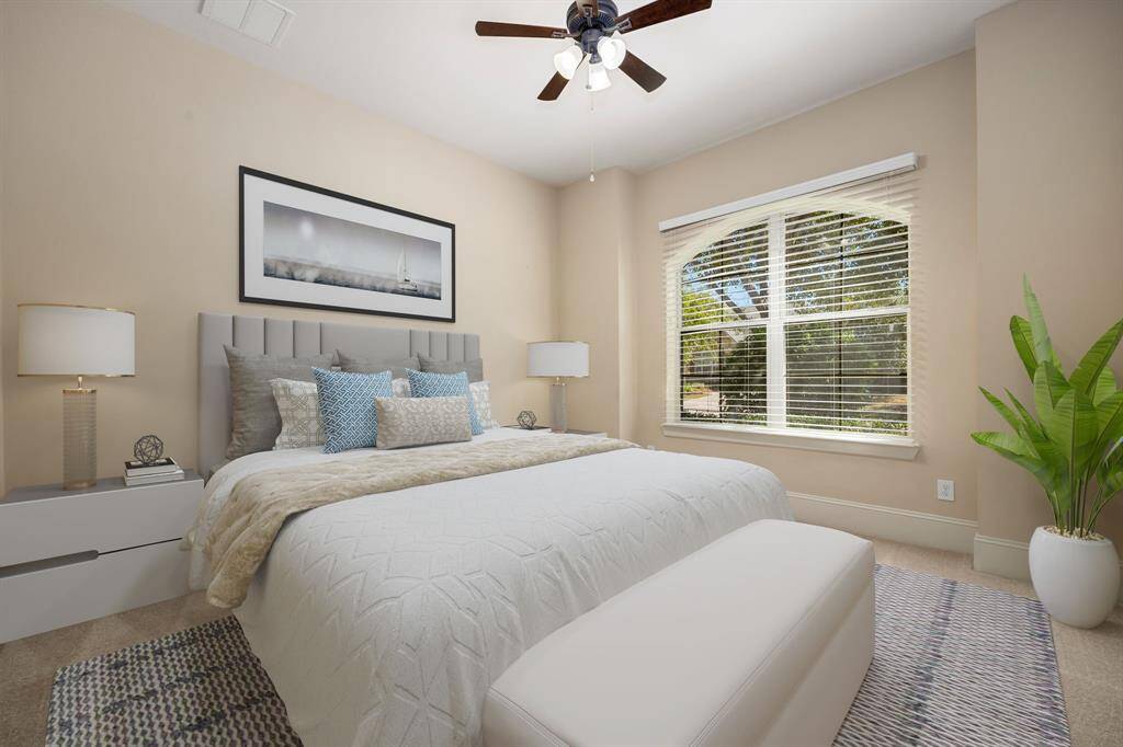 Secondary bedroom features plush carpet, neutral paint, dark stained ceiling fan with lighting and a large arched window with privacy blinds.