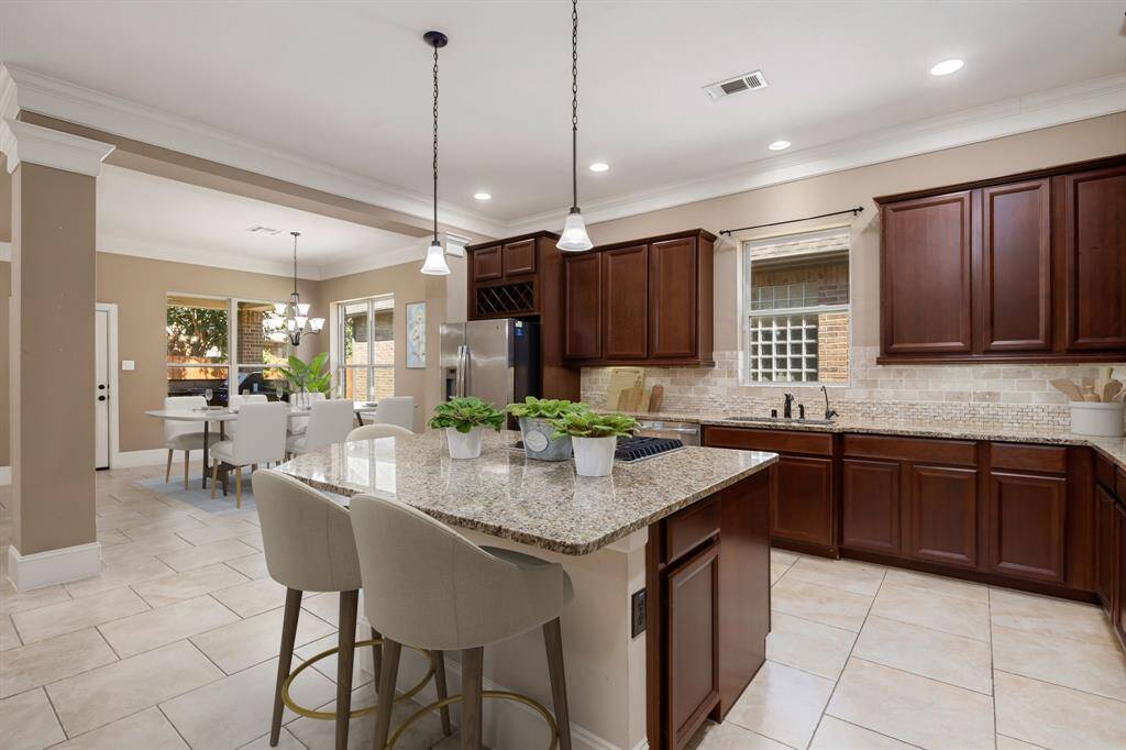 This beautifully designed kitchen exudes elegance and functionality, featuring rich wood cabinetry, sleek granite countertops, and a stylish tile backsplash. The large island provides ample prep space, ideal for cooking and entertaining, while pendant lighting adds a warm ambiance. With an open layout connecting seamlessly to the dining area, this kitchen is perfect for both daily meals and hosting gatherings.
