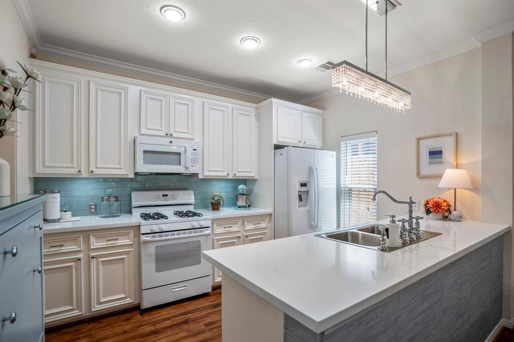 Bright and modern kitchen with white cabinetry and a sleek island.. The space is enhanced by a stylish light fixture and warm wood flooring.