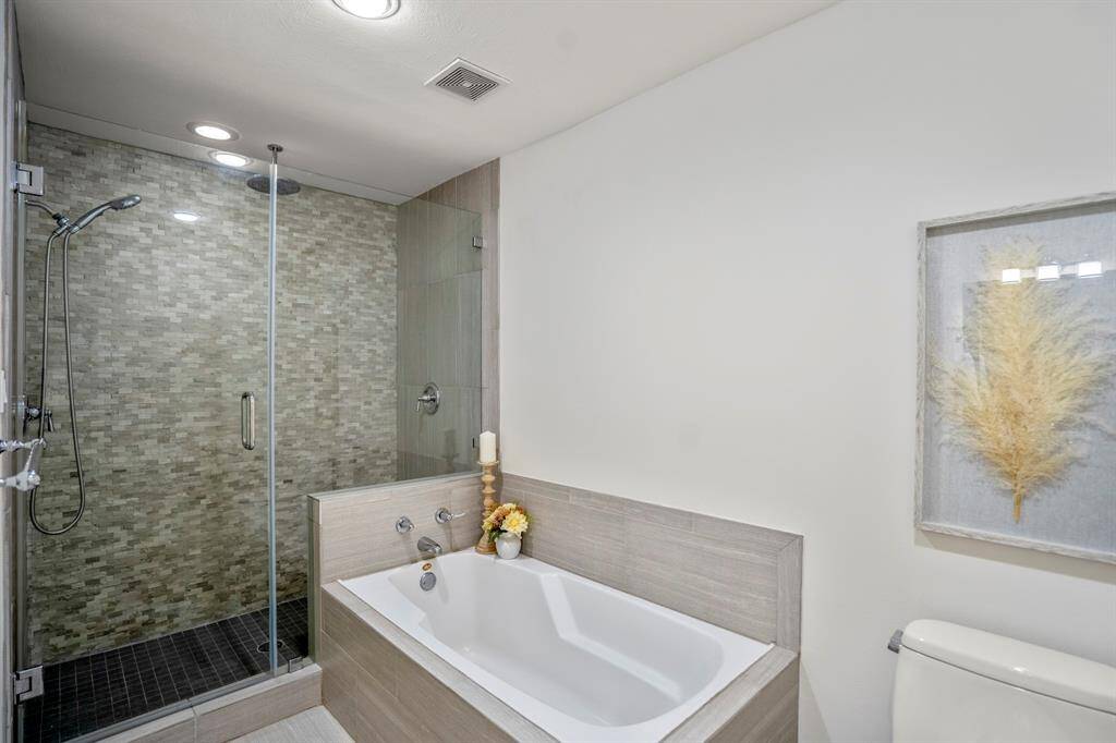 Modern bathroom with a spacious glass-enclosed shower featuring textured tiles, a separate sleek bathtub.