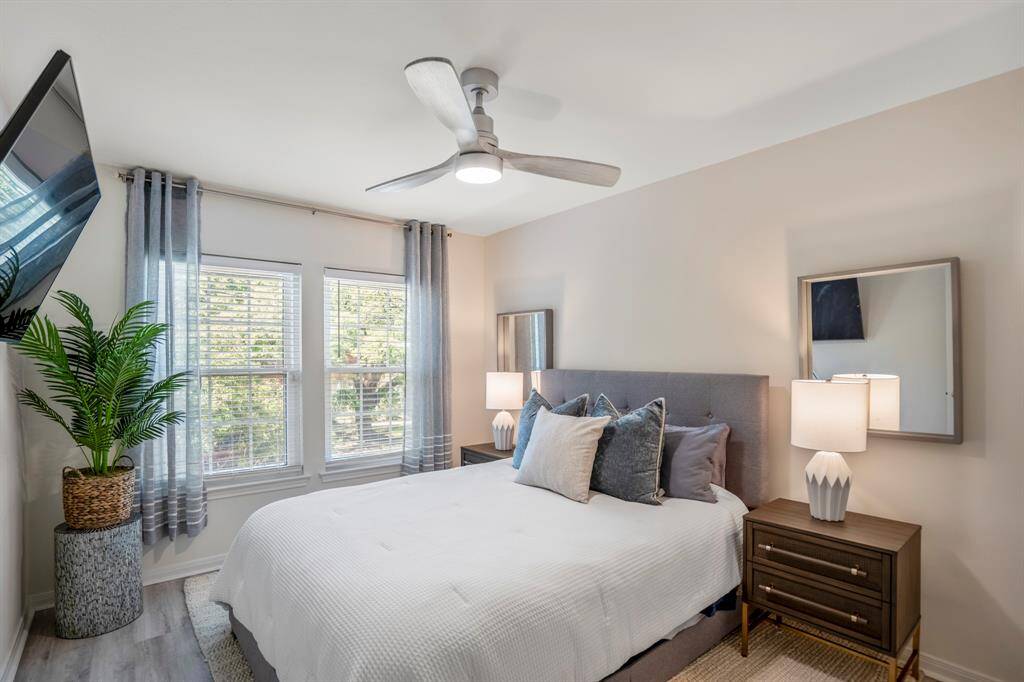 This cozy bedroom features a modern ceiling fan and large windows that offer natural light.