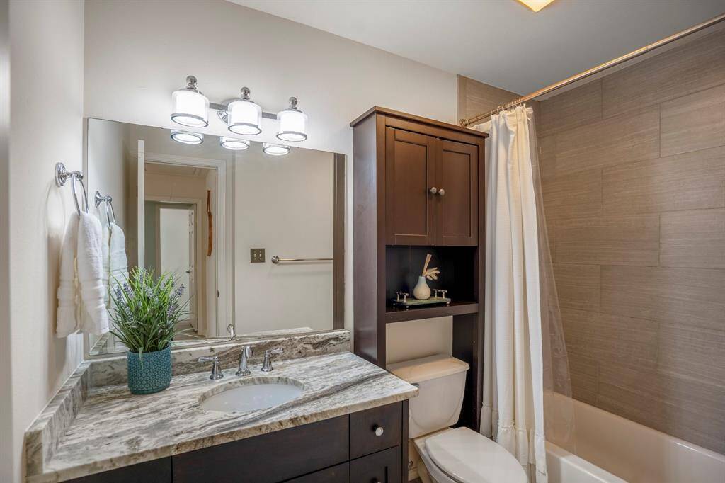 This bathroom features a modern vanity with a marble countertop, a large mirror with bright lighting, and ample storage space. The shower-tub combination is complemented by a sleek tile design.