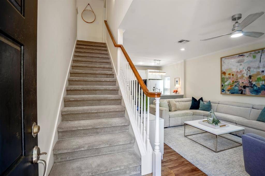 This inviting home features a carpeted staircase and an open living area. The space is well-lit with modern lighting leading into a bright kitchen.