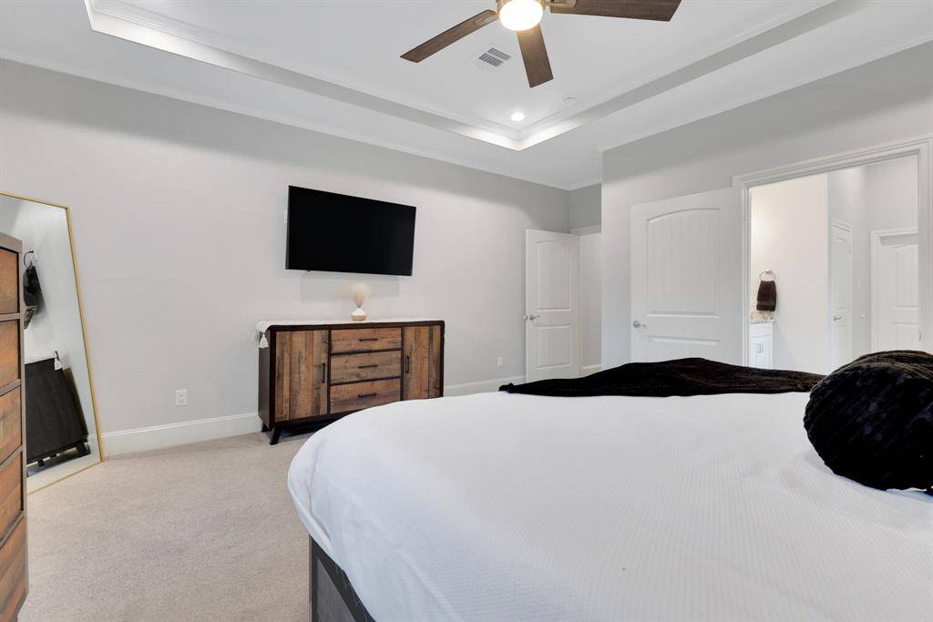 This serene primary suite offers tray ceilings, a luxurious en suite bath, and large windows that showcase the tranquil backyard setting.