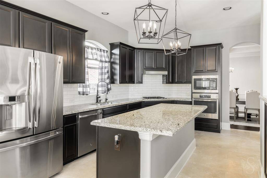 Your kitchen features a central island with seating, stylish pendant lighting, stainless steel appliances, granite countertops, white subway tile backsplash, and a walk-in pantry.