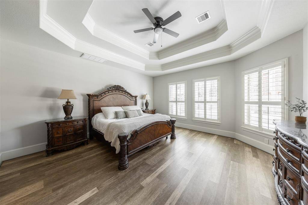 Your primary suite with double tray ceilings, plantation shutters, luxury vinyl plank flooring, and relaxing pool views.