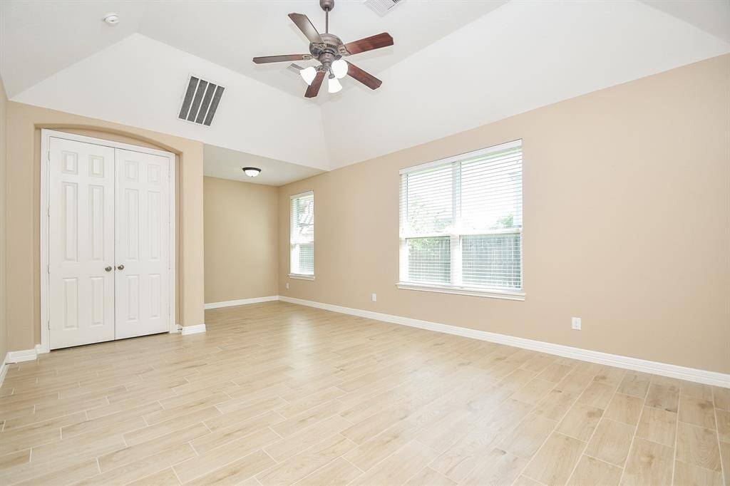Bright and spacious room with vaulted ceiling, light wood like tile  flooring, large window for natural light, and a ceiling fan. Includes a double-door closet. Ideal for a bedroom or office.