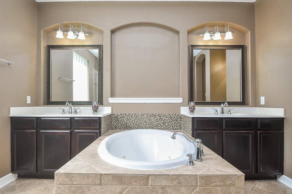 This bathroom features a spacious central bathtub with tiled surround, dual vanities with dark wood cabinets, large mirrors, and elegant lighting fixtures, creating a luxurious and functional space.