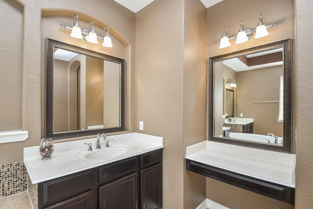 This photo shows a modern bathroom with dual vanities featuring sleek dark wood cabinetry, large mirrors, and stylish light fixtures, offering a clean and sophisticated look.