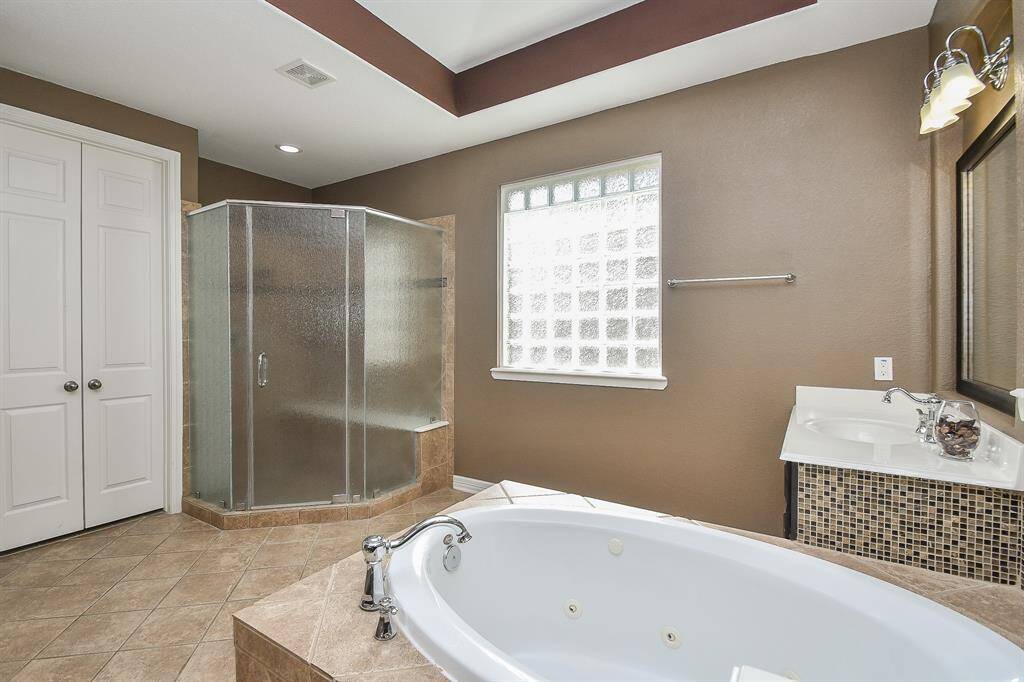 This spacious bathroom features a large soaking tub, a glass-enclosed shower, and a modern vanity. Natural light filters through a frosted window, complementing the warm, neutral wall tones.