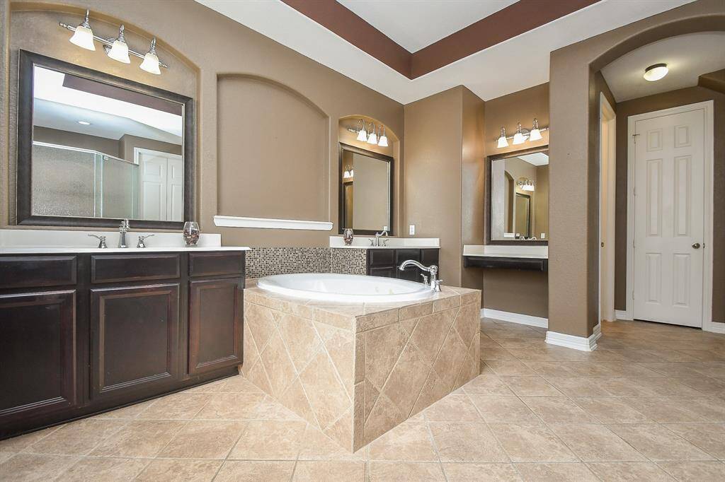 This spacious bathroom features a luxurious soaking tub, dual vanities with elegant dark wood cabinets, and ample natural light. The warm tones and tiled flooring create a cozy, inviting atmosphere.