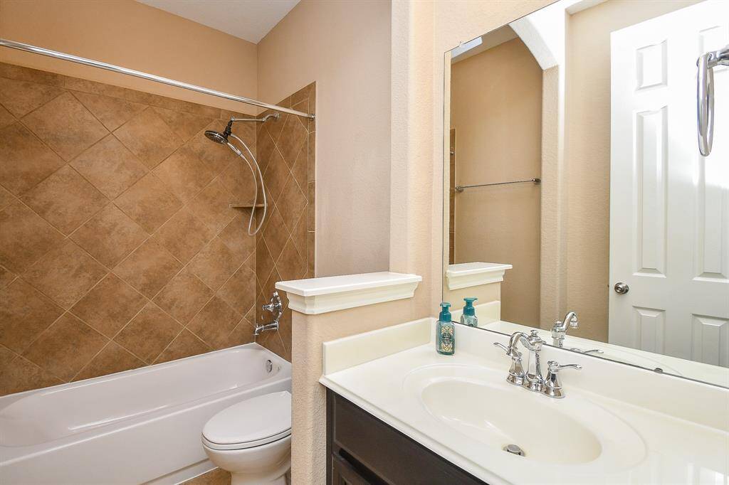 This bathroom features a clean, modern design with a tiled shower and bathtub combo, a sleek white vanity with a mirror, and neutral wall tones for a warm, inviting atmosphere.
