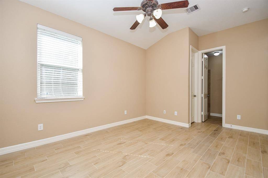 This room features a neutral color scheme with tile flooring and a ceiling fan. It has ample natural light from a window and includes a doorway leading to another area.