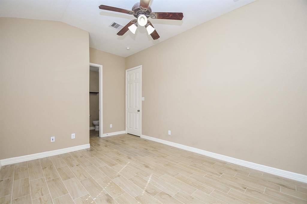This room features neutral-colored walls, wood-look tile flooring, and a ceiling fan. It includes a door leading to an attached bathroom, making it ideal for a bedroom or office space.