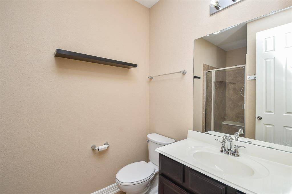 This bathroom features a modern design with a sleek vanity and large mirror. It includes a toilet, a glass-enclosed standing shower, and a neutral color palette. A floating shelf provides additional storage above the toilet.