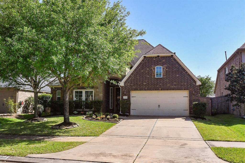 This charming brick home features a spacious driveway, a two-car garage, and a well-maintained front yard with mature trees and shrubs, offering great curb appeal.