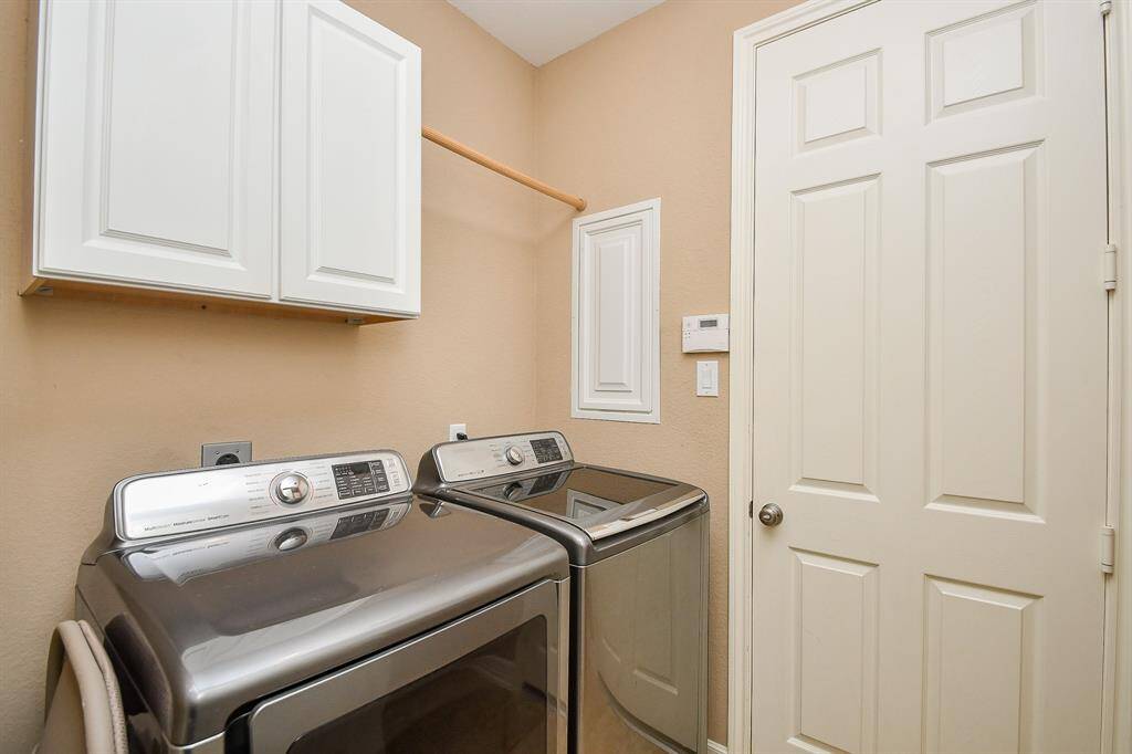 This laundry room features modern appliances, overhead cabinetry for storage, a neutral color scheme, and a door for easy access.