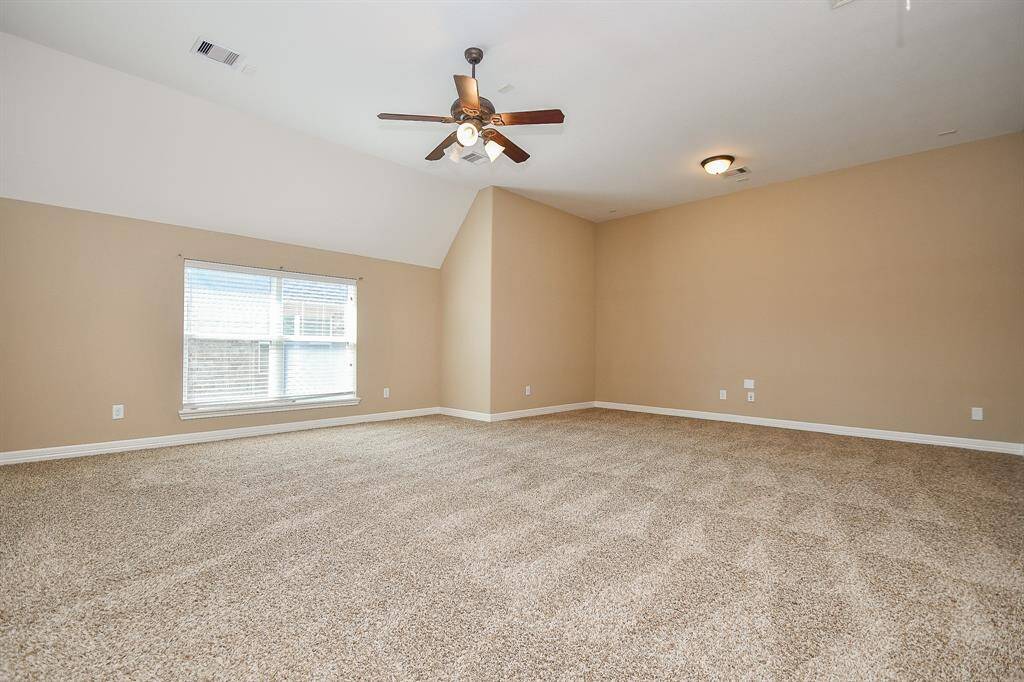 This spacious room features neutral walls and carpet, a ceiling fan for comfort, and ample natural light from a large window, making it versatile for various uses.
