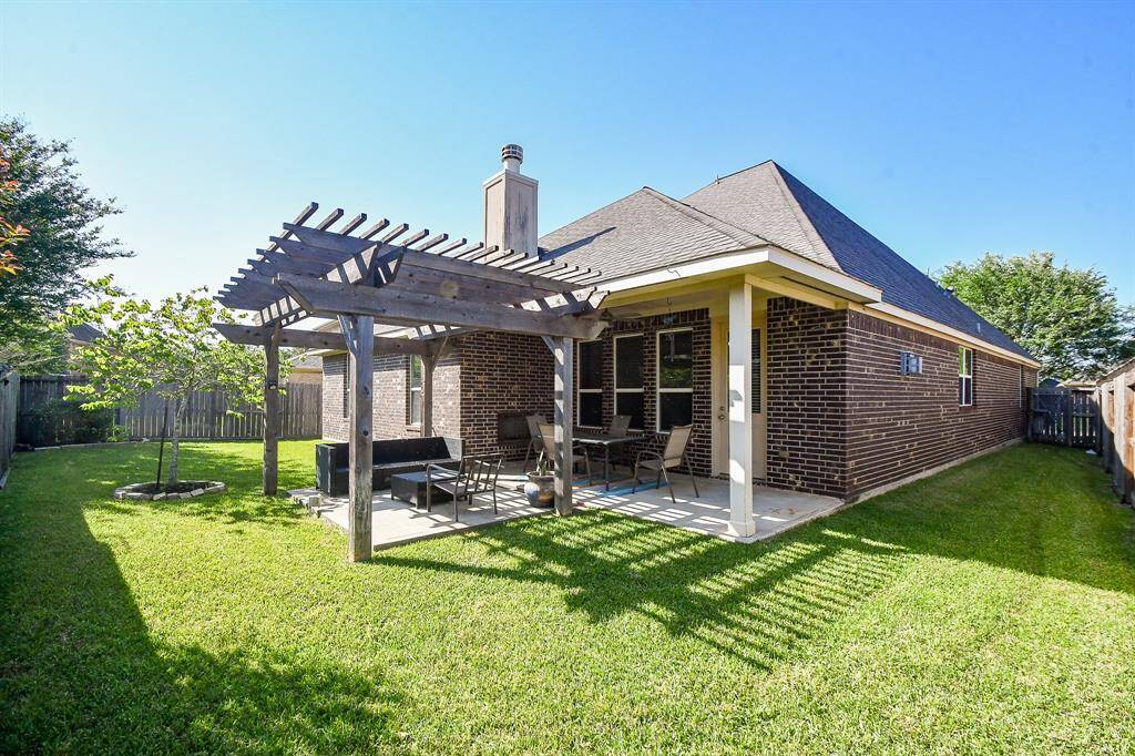 This photo showcases a charming backyard with a well-maintained lawn, a wooden pergola providing shade over a patio area with seating, and a brick exterior house. It's a perfect spot for outdoor relaxation and entertaining.