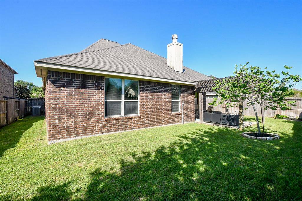 This photo showcases a cozy backyard with a well-maintained lawn, a brick exterior, and a small patio area with a pergola. Ideal for outdoor relaxation and gatherings.