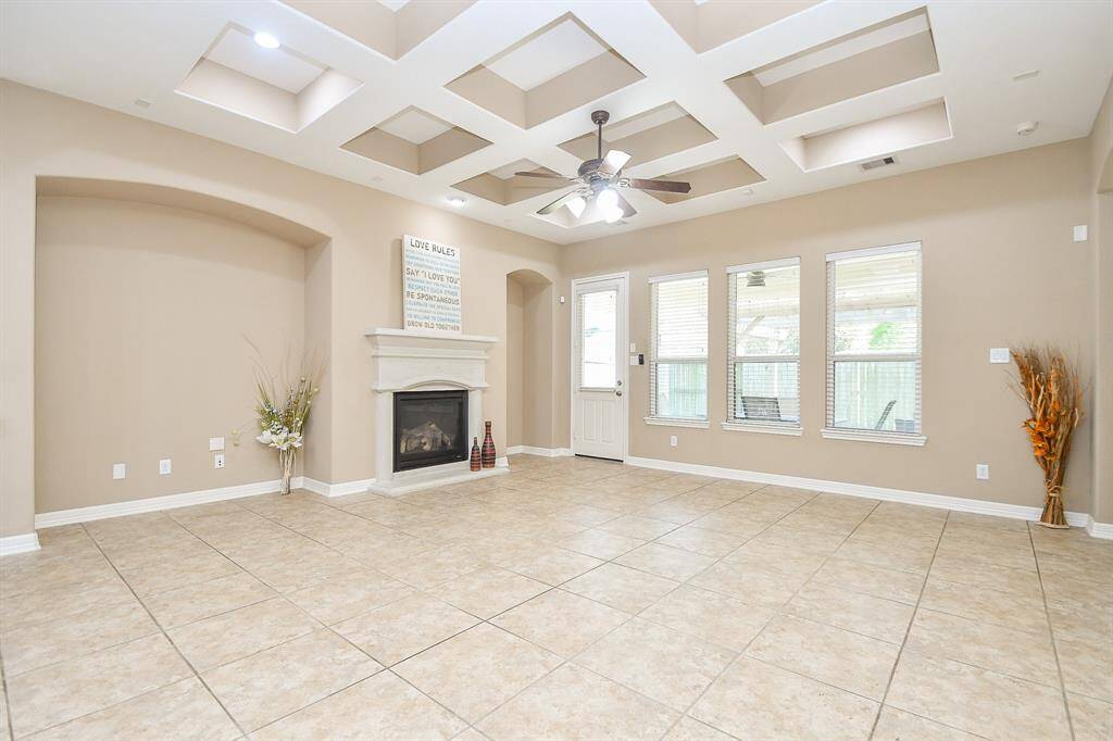 Bright and spacious living room with tiled flooring, a decorative tray ceiling with recessed lighting, and a ceiling fan. Features a cozy fireplace and ample natural light from large windows, with a door leading outside.
