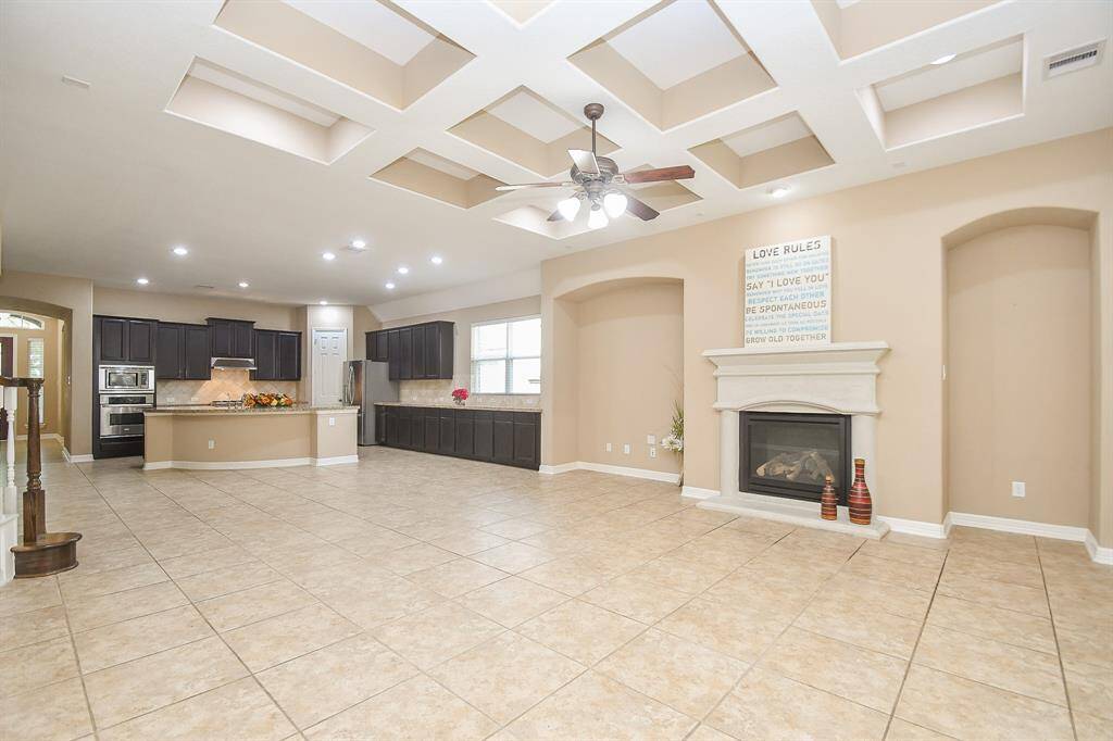This spacious open-concept living area features a modern kitchen with dark cabinetry, stainless steel appliances, and a large island. The room has a cozy fireplace, recessed lighting, and a unique coffered ceiling design. Ideal for entertaining and family gatherings.