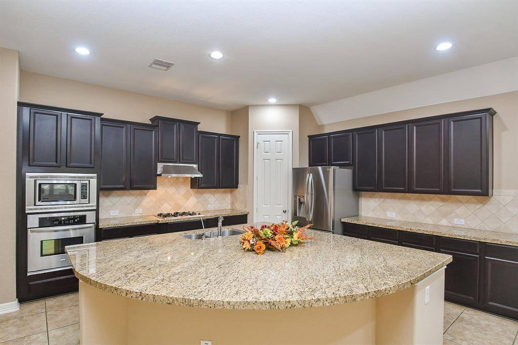 Spacious kitchen featuring dark wood cabinets, stainless steel appliances, and a large granite island with a sink. The room is well-lit with recessed lighting and offers ample counter space for cooking and entertaining.