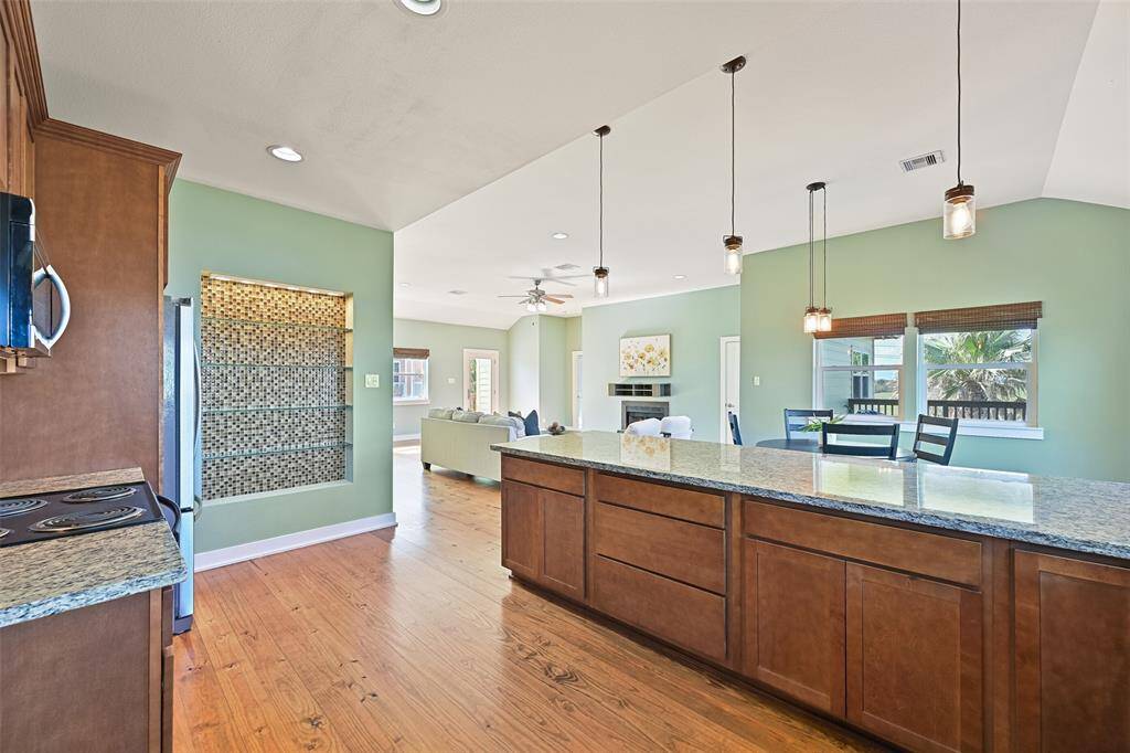 An alternate view of the kitchen focuses on the open floor plan and the inset lighted display shelving built into one wall. Just behind where this photo was taken, there is a walk-in pantry, the utility room, and an interior staircase down to the garage and the bonus storage room.
