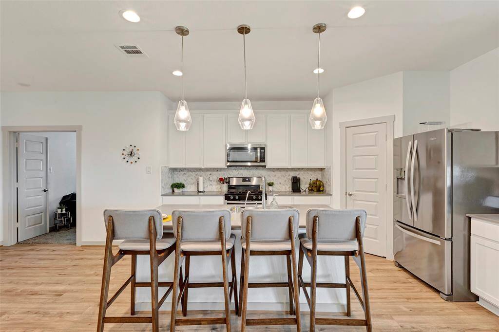 This full view of the kitchen reveals a sleek and tidy space, featuring elegant white cabinetry and modern stainless steel appliances that elevate the overall design.