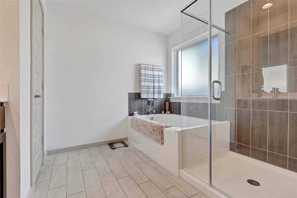 The primary bathroom boasts a luxurious soaking tub, a separate glass-enclosed shower, and a double sink, and a walk-in closet, creating a serene retreat for relaxation and convenience.