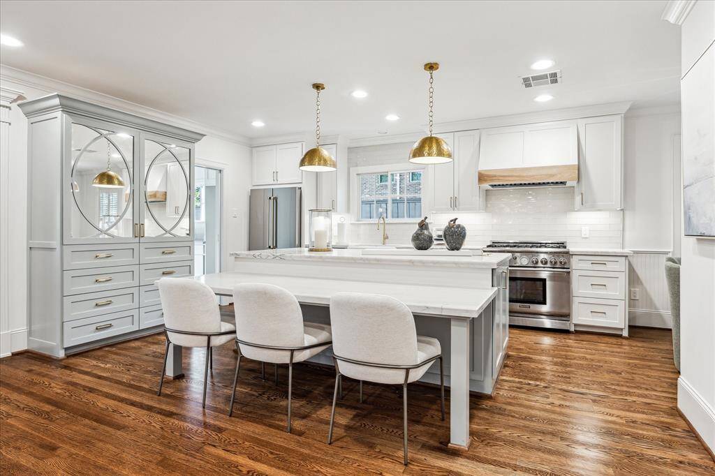 Closer view of the Center island with bar seating/eye catching dual light fixtures, built-in china cabinet, stainless appliances including Viking microwave/Thermador dishwasher/Thermador 6 burner gas oven/range/striking vent hood with cabinet surround.