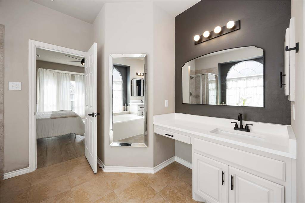 Stylish vanity area in the primary bath, featuring an eye-catching accent wall, upgraded lighting, and modern hardware — all centered around a sleek sink design.