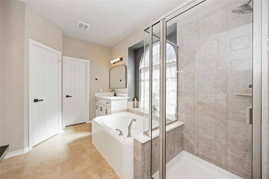The primary bath offers a spa-like retreat with a separate glass-enclosed shower and a relaxing soaking tub, complete with direct access to a spacious walk-in closet.