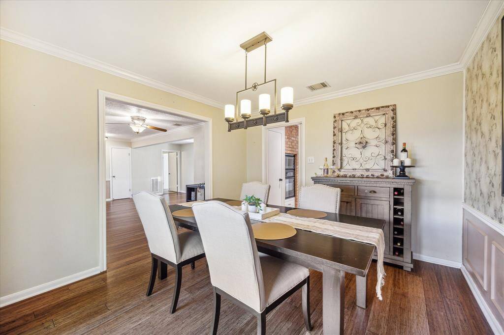 This spacious dining room offers beautiful hardwood flooring, decorator wallpaper and coordinating wainscoting, neutral and designer paint, a chic chandelier, and large windows with amazing views of the front yard.