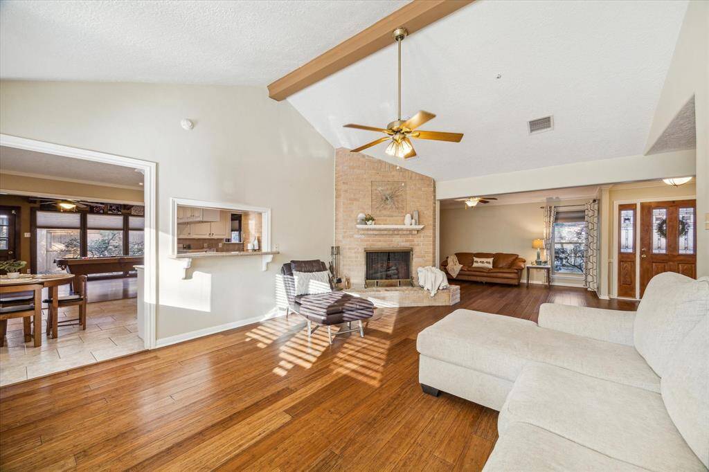 Relax in the bright and airy family room, featuring a vaulted ceiling with a wood beam, an impressive brick fireplace, and a charming built-in window seat. The open layout and abundant natural light make this space perfect for gatherings or quiet evenings in.