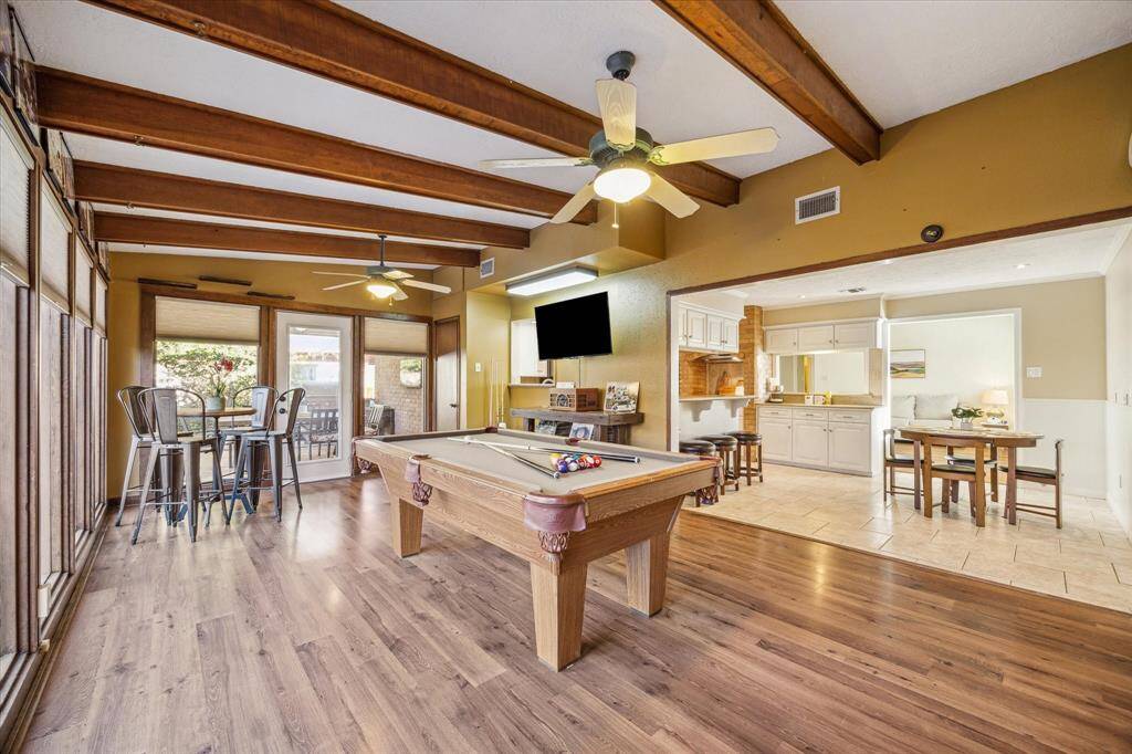 This large sunroom or game room features laminate flooring, stunning wood ceiling beams, and floor-to-ceiling windows that flood the space with natural light. Glass doors provide easy access to the back yard and patio, while its open connection to the breakfast area adds convenience. As one of several living and dining spaces, this room highlights the home’s incredibly flexible floor plan.