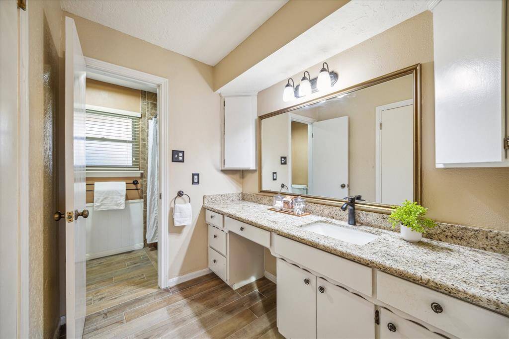 The owner’s ensuite bathroom features an updated vanity with a granite top, an undermount sink with an upgraded fixture, and a framed mirror with vanity lights above.