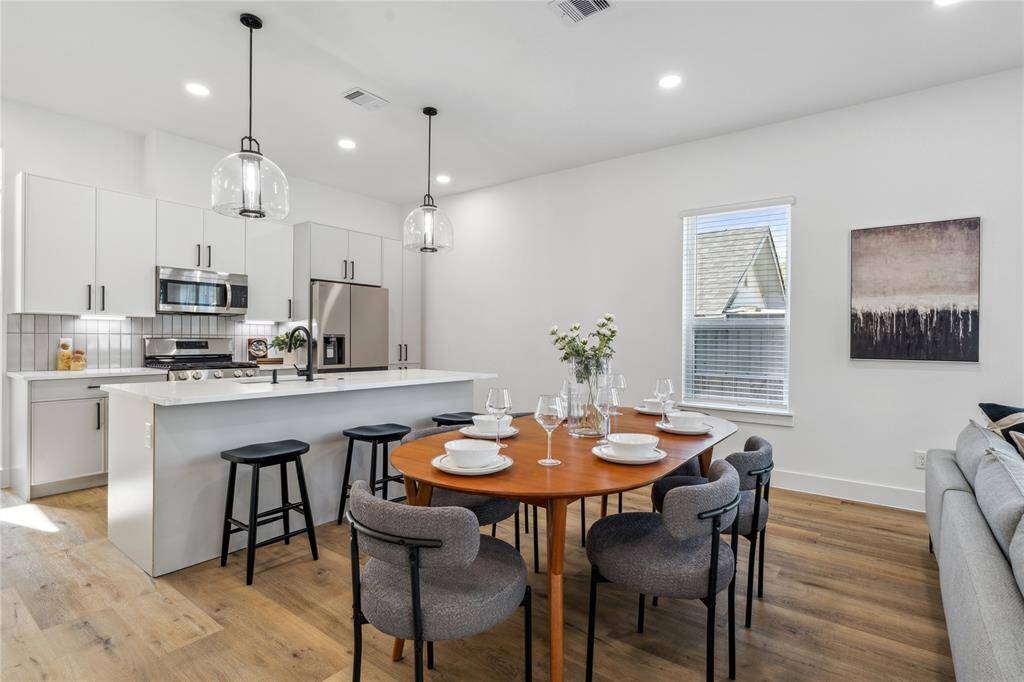 Modern kitchen with sleek white cabinetry, stainless steel appliances, and a spacious island opens up to a dining and living area that allows plenty of space for entertaining.