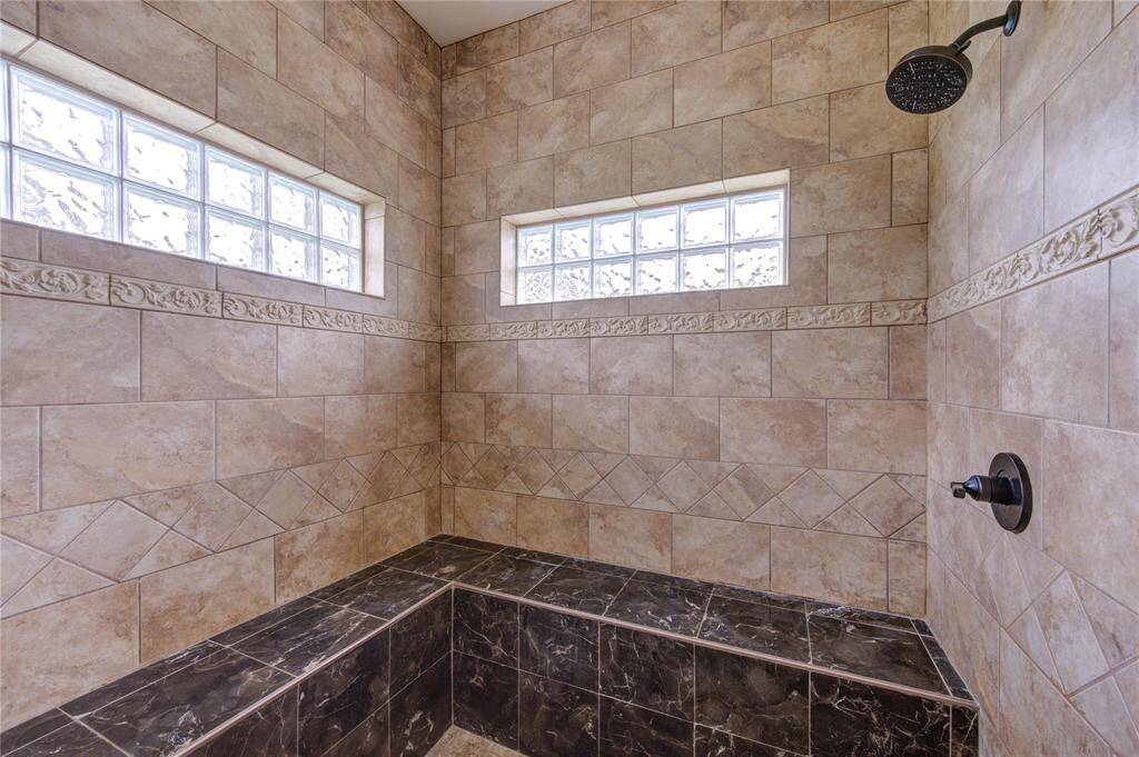Shower with surround tile, dual shower heads, full bench seating, tile flooring and transom windows for natural lighting.