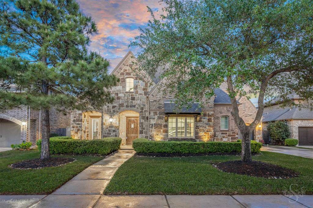 This charming home features a stunning stone facade, lush landscaping, and a welcoming pathway.