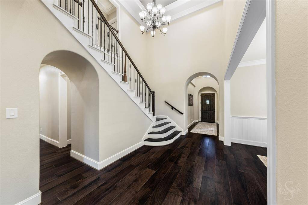 This inviting foyer features high ceilings, a grand staircase with elegant railings, and rich hardwood floors. Arched doorways add a touch of sophistication and lead to other parts of the home, creating a warm and welcoming entrance.