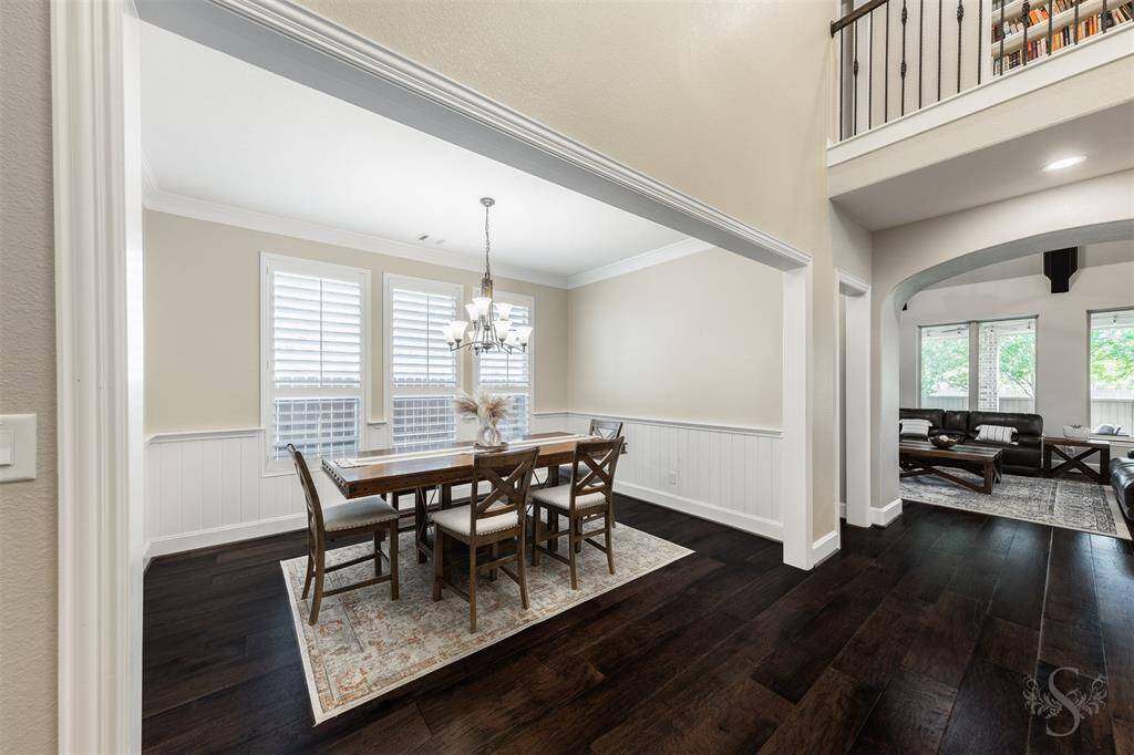 Bright dining area with a modern chandelier, large windows with plantation shutters, and dark hardwood flooring.