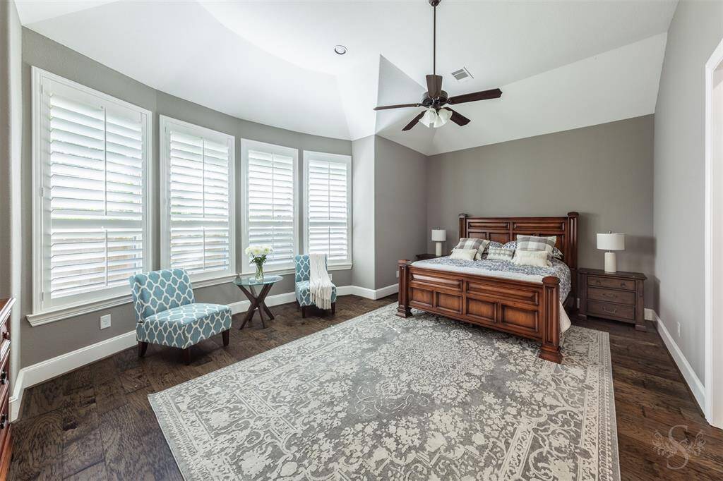 This spacious primary bedroom features a vaulted ceiling, large windows with plantation shutters, and elegant hardwood flooring.