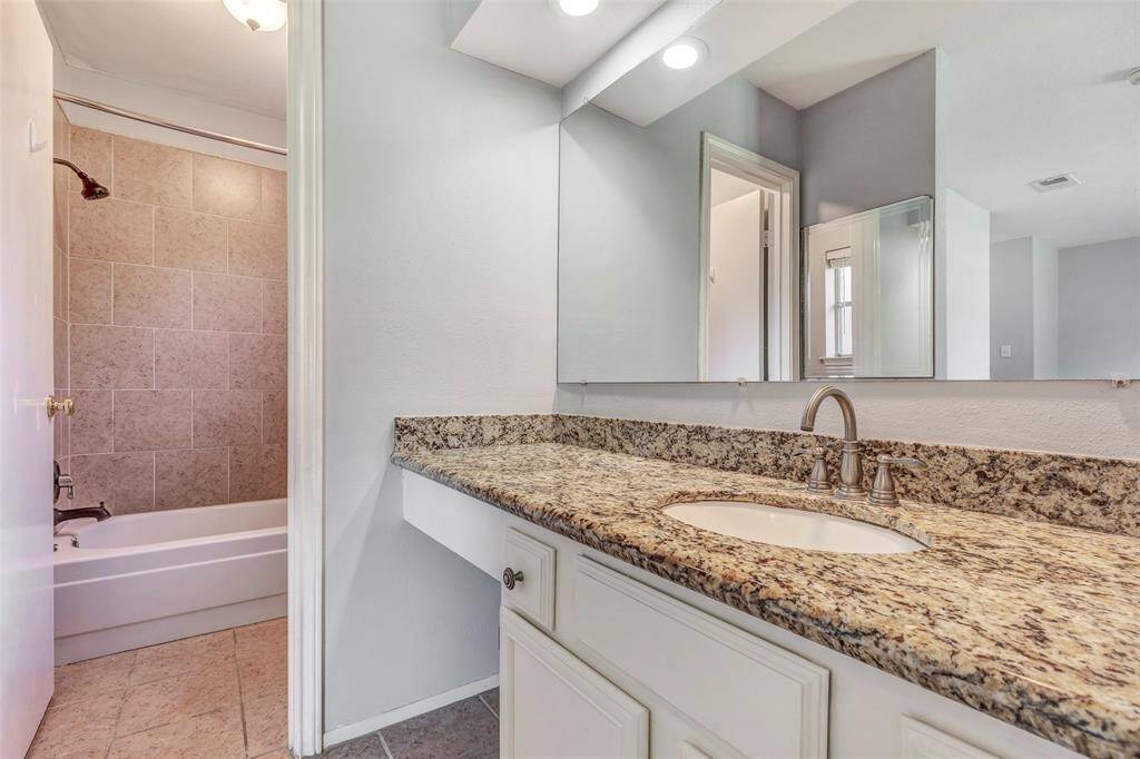 The primary bathroom boasts a tub and shower combo, complemented by a large vanity mirror and elegant granite countertops, offering a blend of functionality and luxury.